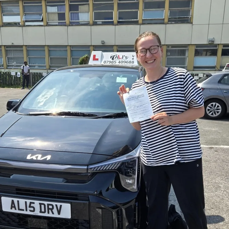 A smiling new driver in a striped top with a pass certificate, next to the front of the learner car