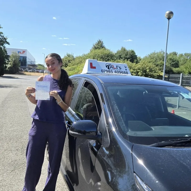 A new driver holding up a pass certificate beside the learner car on a sunny day