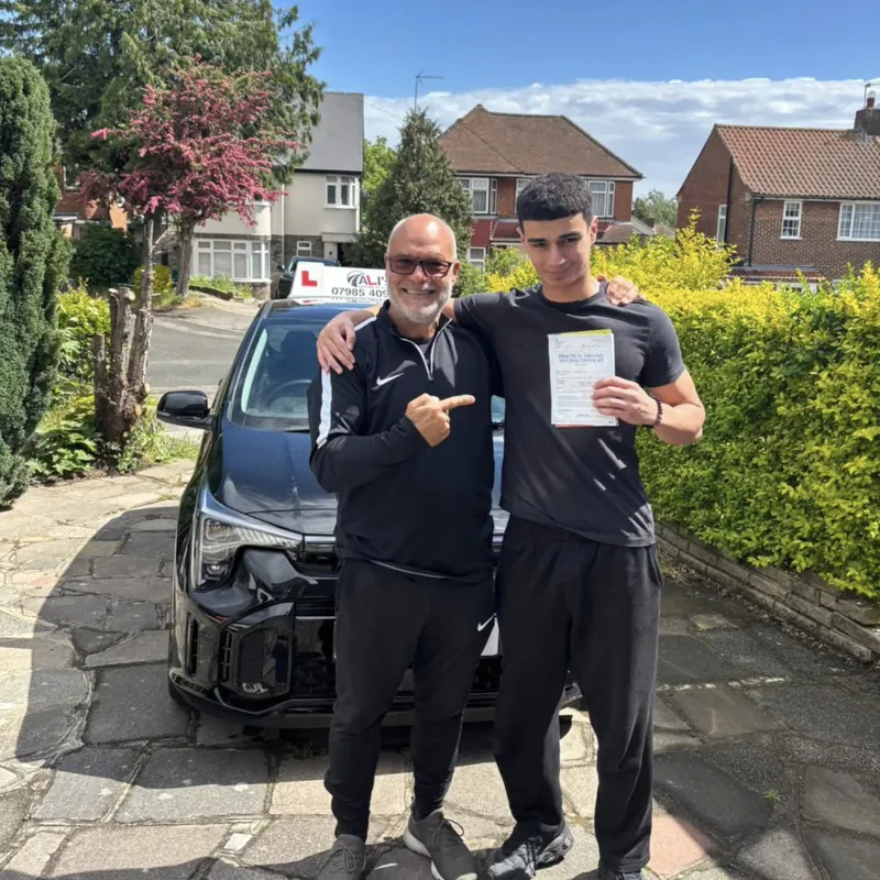 Two people standing by the learner car on a residential street, one holding a pass certificate