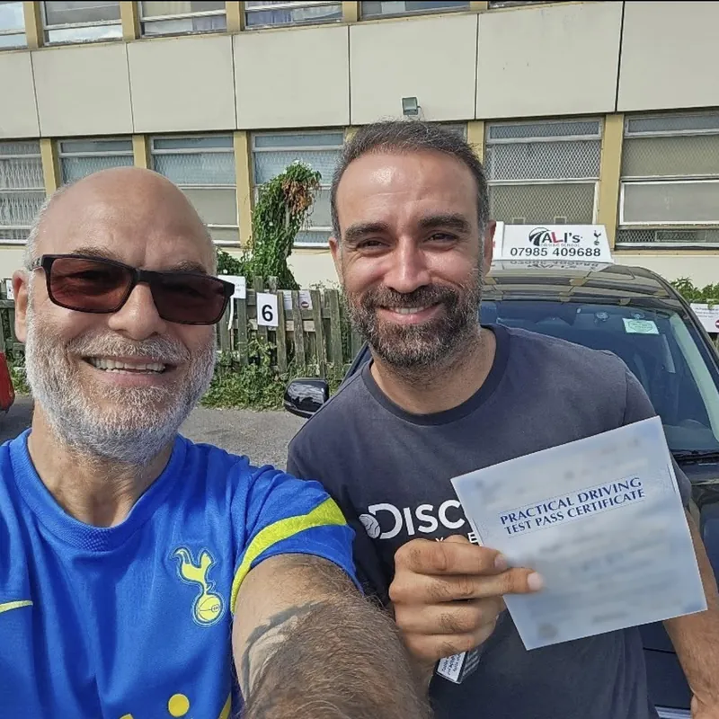 A selfie of two people, one holding up a practical driving test pass certificate