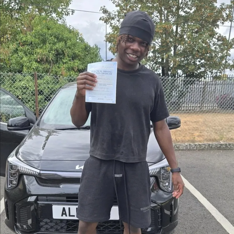 A new driver in a beanie holding up a pass certificate in front of the learner car