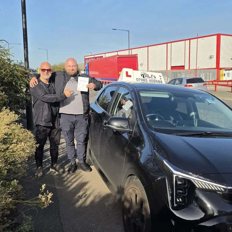 Two people by the learner car in a sunny car park, one holding a pass certificate
